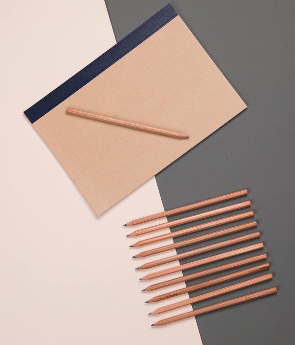 Top view set of various multicolored pencils placed on pink and gray table in row near sketchbook